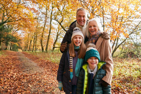 Portrait Of Grandparents With Grandchildren Enjoying Walk Along Autumn Woodland Path Togetherの写真素材