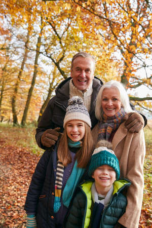 Portrait Of Grandparents With Grandchildren Enjoying Walk Along Autumn Woodland Path Together