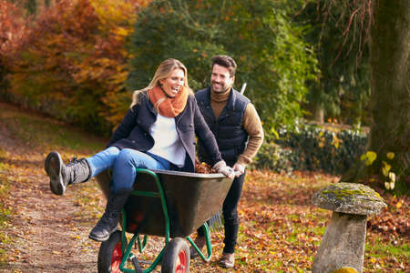 Man Pushing Woman In Wheelbarrow As Couple Rake Autumn Leaves From Garden Togetherの写真素材