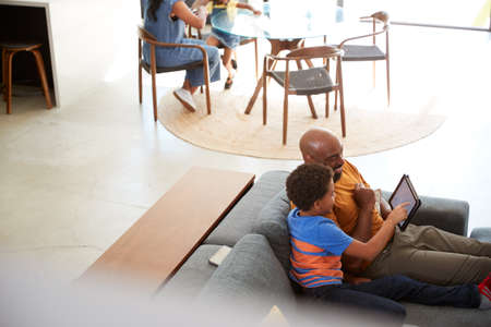 African American Family At Home With Father And Son Sitting On Sofa At Home Using Digital Tablet