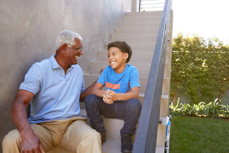 Grandfather With Grandson Sitting On Steps And Talking Outdoors At Homeの写真素材