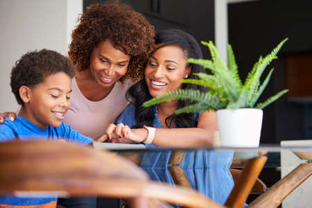 Grandmother With Mother Helping Grandson To Do Homework On Digital Tablet