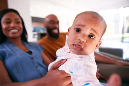 Portrait Of Smiling African American Parents Cuddling Baby Daughter Indoors On Sofa At Homeの写真素材