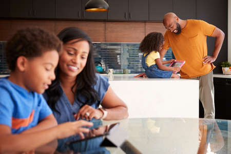 African American Parents Helping Children Studying Homework On Digital Tablets In Kitchen
