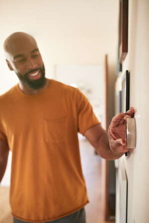 Man Adjusting Digital Central Heating Thermostat At Homeの写真素材