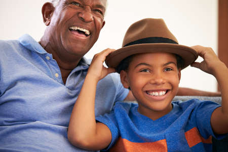 African American Grandfather And Grandson Family Sitting On Sofa With Boy Wearing Hatの写真素材