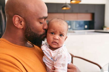 Smiling Stay At Home African American Father Cuddling And Playing With Baby Daughter Indoors At Home