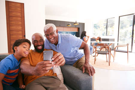 Multi-Generation Male African American Family On Sofa At Home Posing For Selfie On Mobile Phoneの写真素材