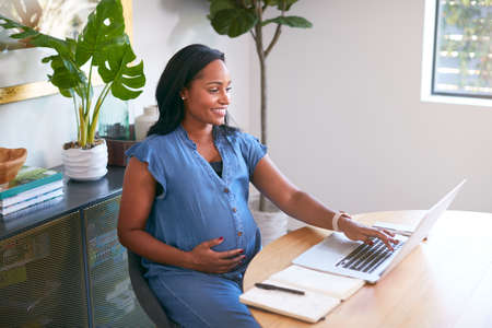 Pregnant African American Woman Using Laptop At Table Working From Homeの写真素材