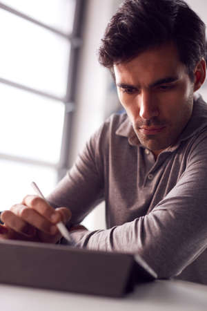 Businessman Working From Home Drawing On Digital Tablet Using Stylus Penの写真素材