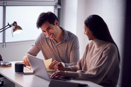 Businesswoman Working On Laptop At Desk Collaborating With Male Colleagueの写真素材