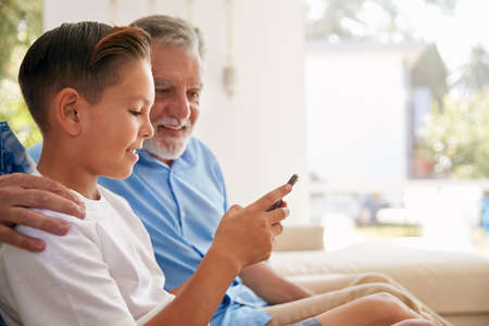 Hispanic Grandson Showing Grandfather How To Use Mobile Phone At Home