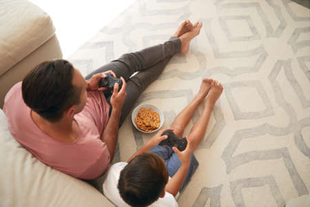 Overhead View Of Hispanic Father And Son Sitting On Floor At Home Playing Video Game Together