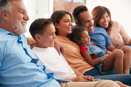 Multi-Generation Hispanic Family Relaxing At Home Sitting On Sofa Watching TV Togetherの写真素材