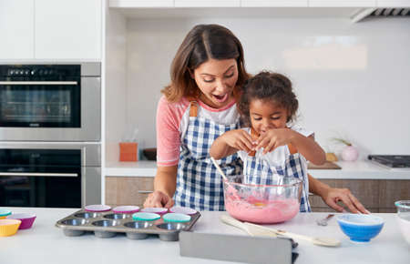 Hispanic Mother And Daughter Having Fun In Kitchen At Making Cake Together