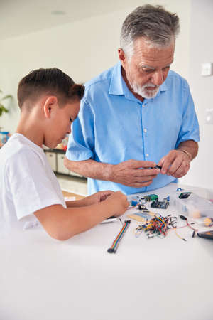 Hispanic Grandson And Grandfather Building Robot From Electronic Components At Home Togetherの写真素材