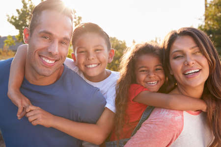 Portrait Of Hispanic Family Relaxing In Garden At Home With Parents Giving Children Piggybacksの写真素材