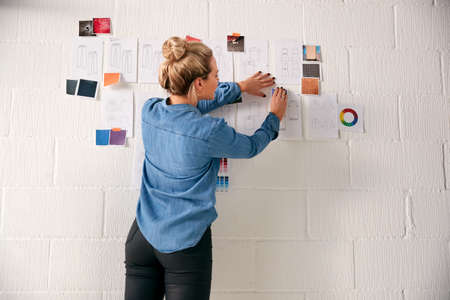 Rear View Of Businesswoman Looking At Designs On Wall In Start Up Fashion Businessの写真素材