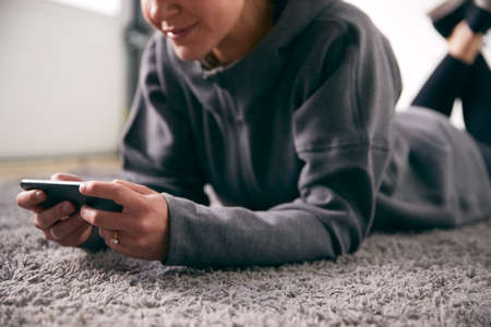 Close Up Of Woman At Home Looking At Social Media And Text Messages On Mobile Phone Lying On Carpetの写真素材