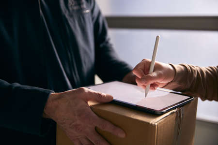 Woman Signing For Courier Delivery To Office Using Digital Tabletの写真素材