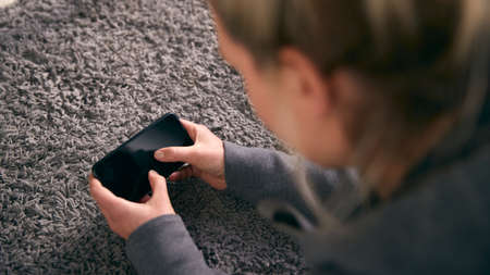 Overhead Shot Of Woman Looking At Screen With Copy Space On Mobile Phone Lying On Carpet