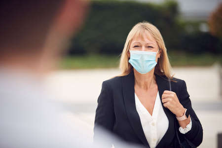 Mature Businesswoman Wearing PPE Face Mask Meeting Colleague In Street During Health Pandemicの写真素材