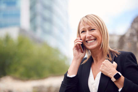 Mature Businesswoman Talking On Mobile Phone As She Walks Through City Streetの写真素材