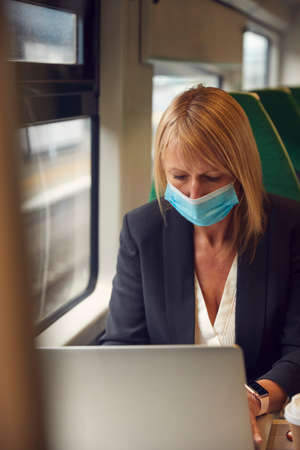 Businesswoman On Train Working On Laptop Wearing PPE Face Mask During Health Pandemicの写真素材