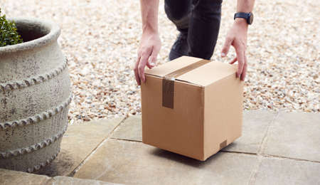 Close Up Of Delivery Driver Putting Package On Doorstep Outside Houseの写真素材