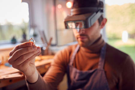 Close Up Of Male Jeweller Looking At Ring Through Headband Magnifiers In Studioの写真素材
