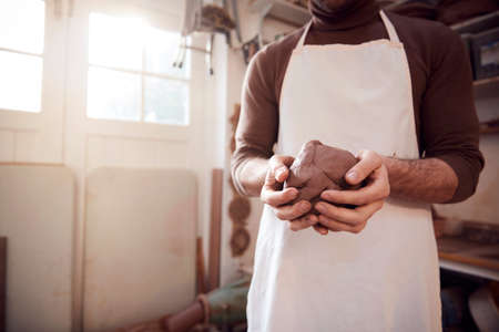 Close Up Of Male Potter Wearing Apron Holding Lump Of Clay In Ceramics Studioの写真素材