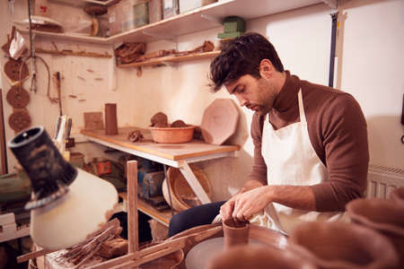 Male Potter Shaping Clay For Pot On Pottery Wheel In Ceramics Studioの写真素材