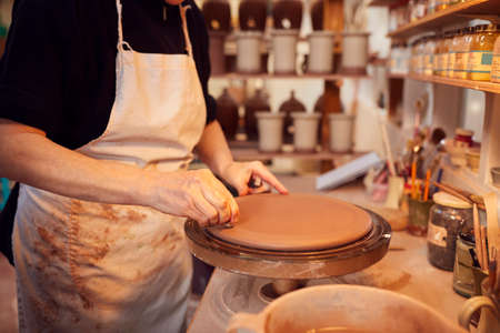 Close Up Of Potter Putting Manufacturers Stamp Onto Bottom Of Clay Plate In Ceramics Studio