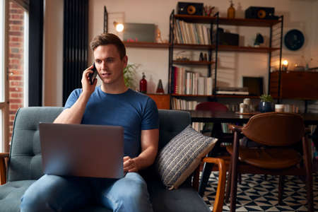 Man Working From Home On Laptop Making Call On Mobile Phoneの写真素材