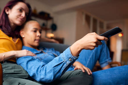 Loving Same Sex Female Couple Lying On Sofa At Home Watching TV And Relaxing Together