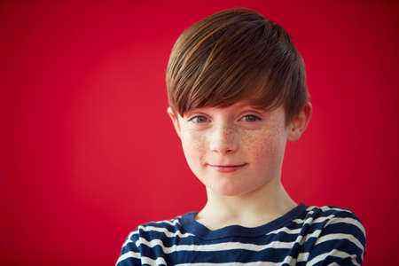 Portrait Of Young Boy Against Red Studio Background Smiling At Cameraの写真素材