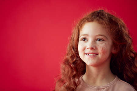 Portrait Of Girl With Long Red Hair Against Red Studio Background Smiling At Camera