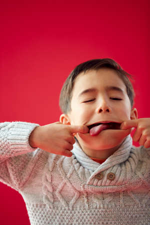 Portrait Of Young Boy Against Red Studio Background Pulling Funny Faces At Cameraの写真素材