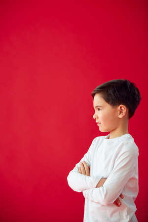 Portrait Of Young Boy With Folded Arms Against Red Studio Background Smiling At Cameraの写真素材