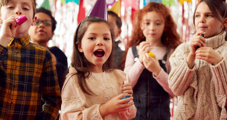 Group Of Children Celebrating At Birthday Party With Paper Hats And Party Blowers