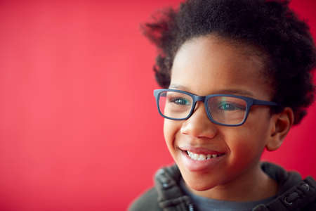 Portrait Of Smiling Young Boy Wearing Glasses Against Red Studio Background