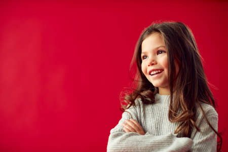 Portrait Of Young Girl With Folded Arms Against Red Studio Background Smiling At Camera