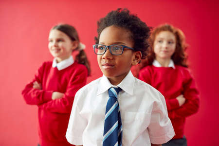 Group Of Elementary School Pupils Wearing Uniform Folding Arms Against Red Studio Backgroundの写真素材
