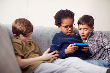 Group Of Young Boys Gaming Together On Hand Held Devices At Home
