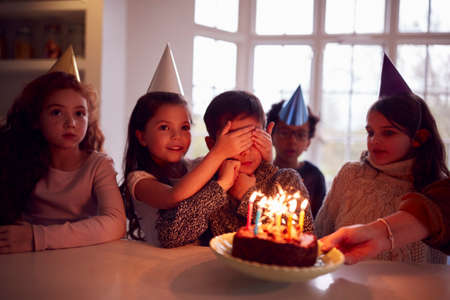 Boy Celebrating Birthday With Group Of Friends At Home Being Given Cake Decorated With Sparklerの写真素材