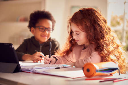 Two Children Sitting At Kitchen Counter Doing Homework Using Digital Tabletの写真素材