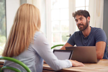 Couple With Laptop Sitting At Table Working From Home Together