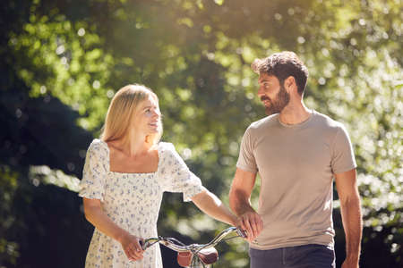 Couple Walking Along Summer Countryside Path Pushing Bike