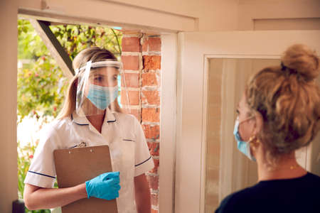 Female Health Worker Wearing Mask And Visor Visiting Woman At Homeの写真素材