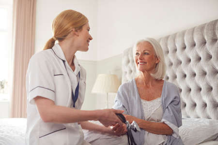 Female Doctor Making Home Visit To Senior Woman In Bedroom For Blood Pressure Checkの写真素材